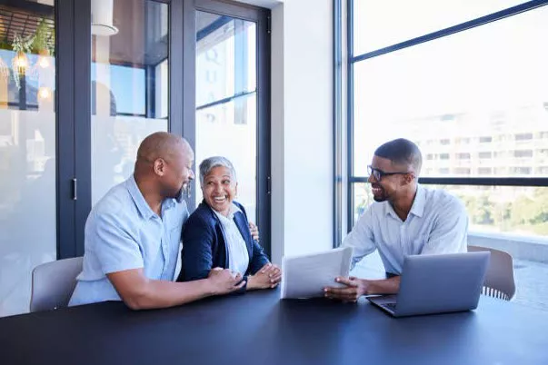 A couple smiling across the table from their advisor, plan on the laptop between them