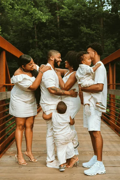 A family dressed in white standing together on a wooden bridge in the woods, smiling